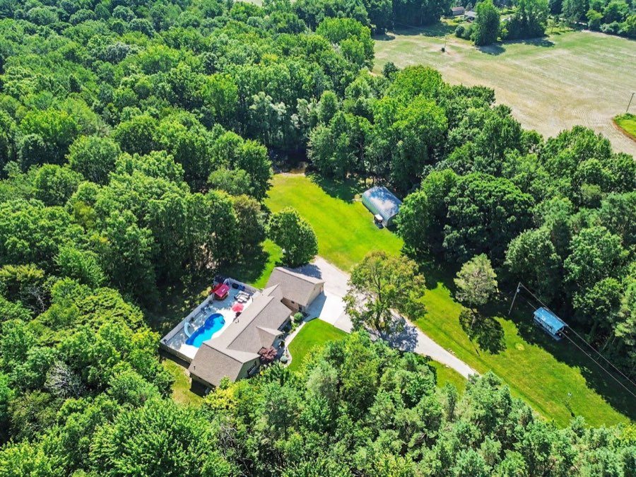 Aerial view of the home, inground pool, Quonset steel outbuilding, lawn, and wooded setting