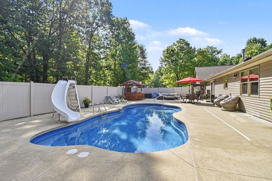 Heated saltwater inground pool with slide, patio, tiki bar, and privacy fence
